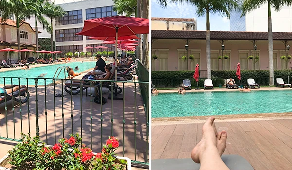 Imagem de uma piscina em um ambiente ao ar livre com espreguiçadeiras, guarda-sóis vermelhos e pessoas relaxando ao redor, ideal para fotos de lazer e descanso.