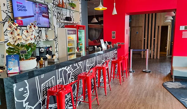 Interior de uma cafeteria moderna com bebedouro, balcão decorado e cadeiras vermelhas, ideal para quem busca um ambiente acolhedor