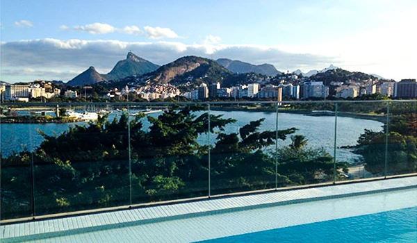 Vista panorâmica do Rio de Janeiro com montanhas, baía e cidade ao fundo, vista de uma área de lazer com piscina e decoração com vidro.