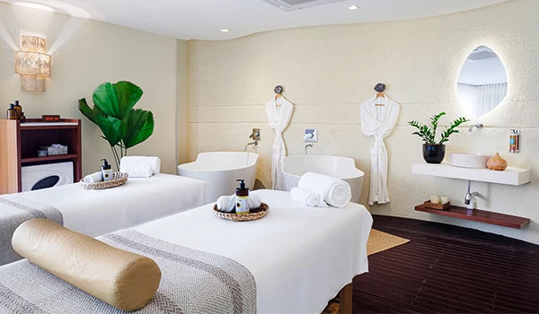 Spa de relaxamento com duas macas de massagem, decoração minimalista, plantas verdes, iluminação suave e ambiente tranquilo para bem-estar.
