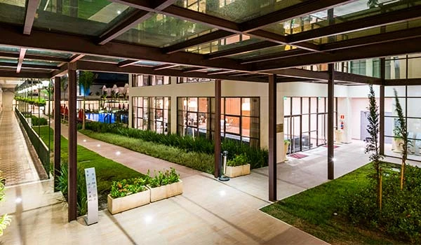 Imagem de um espaço moderno ao ar livre com jardins bem cuidados, área de caminhada e cobertura de vidro, ideal para lazer e convivência em ambientes urbanos.