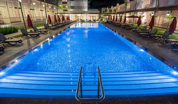 Piscina iluminada à noite em um ambiente moderno, com espreguiçadeiras e guarda-sóis ao redor, ideal para lazer e relaxamento em área residencial ou hotel
