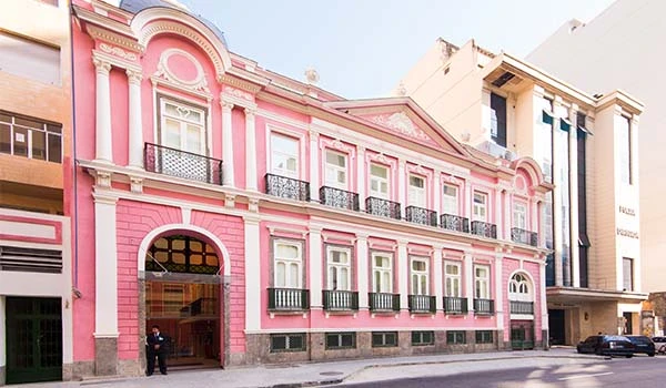 Fachada de edifício clássico com detalhes arquitetônicos em rosa e branco, localizado na cidade, ideal para hospedagem no Rio de Janeiro.