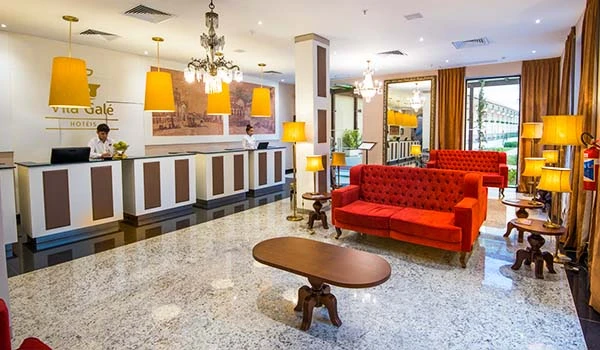 Lobby de hotel com decoração cativante, incluindo sofá vermelho, iluminação aconchegante, recepção moderna e ambientes bem iluminados.