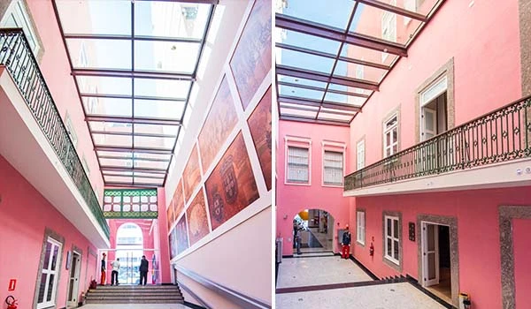 Imagem de um corredor interior com teto de vidro em um prédio moderno com paredes rosa, detalhes em branco e acesso a áreas internas com escadas e janelas. Hotel Histórico no Rio de Janeiro.