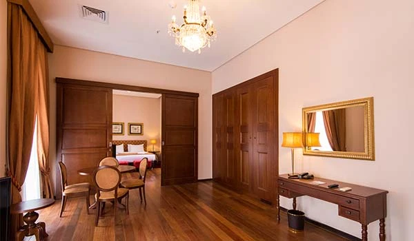 Imagem de um quarto de Hotel Histórico no Rio de Janeiro, com decoração clássica, cama de casal, mesa de jantar com cadeiras e espelho dourado, ideal para hospedagem confortável.