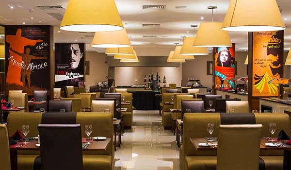 Imagem de um restaurante elegante com mesas bem decoradas, poltronas confortáveis, iluminação suave e banners culturais nas paredes.