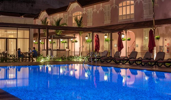 Piscina de hotel luxuoso à noite com espreguiçadeiras, guarda-sóis vermelhos e decoração elegante. Hotel Histórico no Rio de Janeiro.