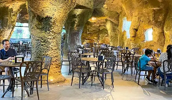 Restaurante aconchegante em cavernas com mesas e cadeiras, ideal para refeições ao ar livre e com ambiente natural e iluminado, perfeito para experiências gastronômicas