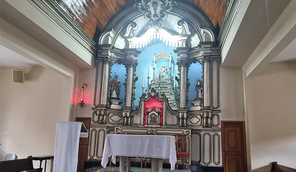 Imagem de um altar de igreja com detalhes ornamentais em estilo clássico, featuring esculturas religiosas, uma cruz e uma pintura no fundo. O altar é decorado com elementos tradicionais de uma igreja católica, sugestivo de um espaço religioso interno com detalhes decorativos especiais.