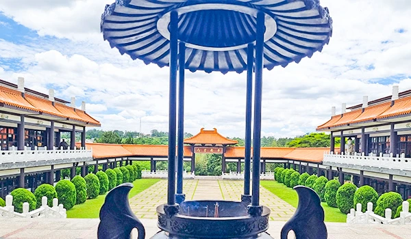 Imagem de uma estrutura incenso ao ar livre em um jardim bem cuidado, cercado por árvores e edifícios com telhados tradicionais no Templo Zu Lai.