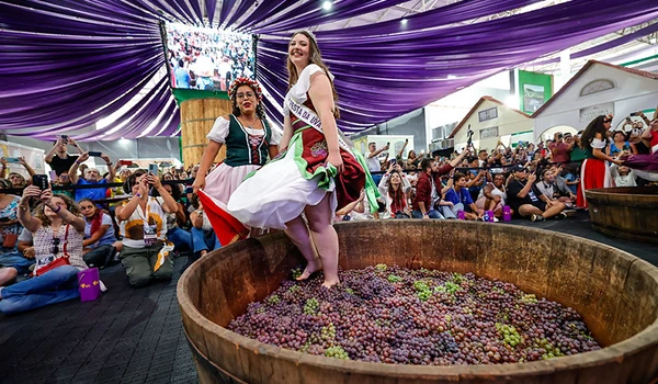 39ª Festa da Uva e 10ª Expo Vinhos Rainha, tradição de pisar uvas em um barril durante festival, cercadas por uma multidão animada. Uma das atividades do Turismo Rural em Jundiaí.