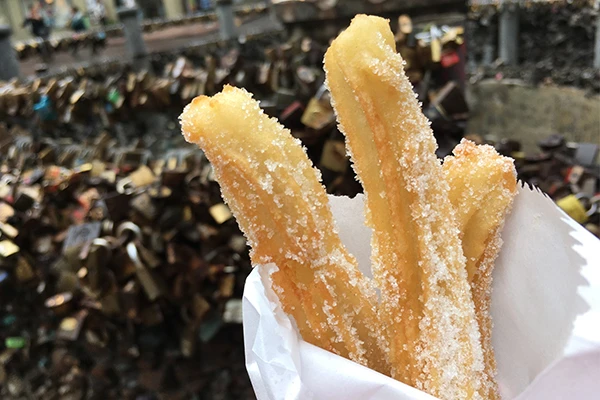 Churros crocantes com açúcar de confeiteiro em um cenário ao ar livre, valorizando a culinária típica e a experiência de saborear doces tradicionais.