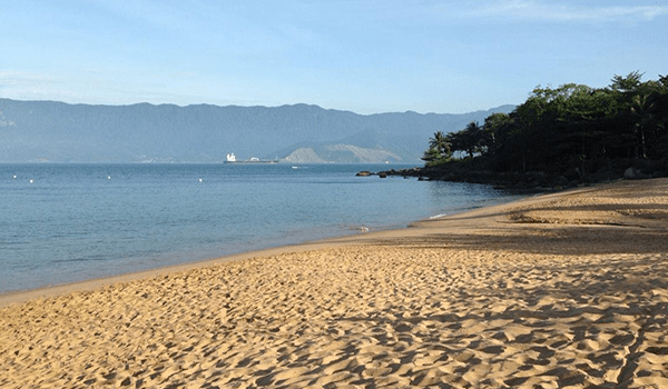 Foto de praia com areia e vista da Serra e da vegetação no Litoral Norte de São Paulo.