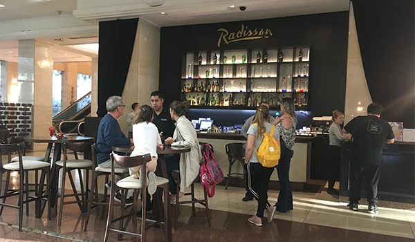 Imagem do lobby do hotel Radisson, com várias pessoas conversando e aproveitando a área de bar na recepção, ambiente sofisticado e acolhedor.