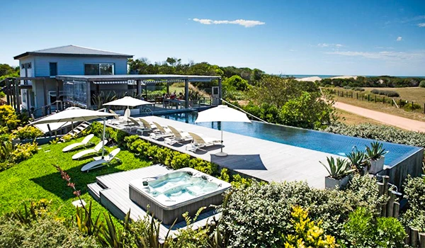 Vista de uma linda casa de veraneio com piscina infinita ao ar livre, cercada por áreas verdes, em um dia ensolarado, perfeita para lazer e descanso ao ar livre.