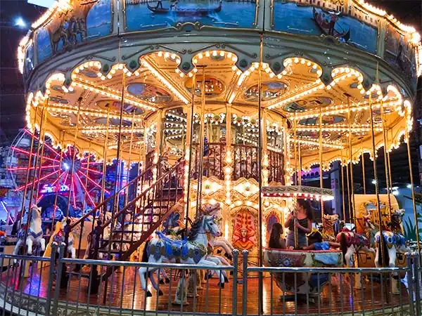 Carrossel iluminado em parque de diversões, com cavalos de madeira e decoração vibrante, proporcionando uma experiência encantadora para crianças e adultos.