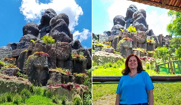 Deusa Rodrigues em frente à escultura de rochas na natureza, com céu azul claro e vegetação ao redor, evidenciando a beleza do local.