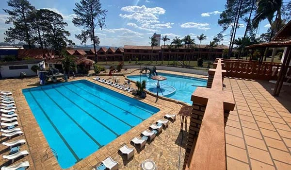 Vista ampla da piscina em um resort, com espreguiçadeiras, árvores e céu azul. Ideal para relaxar e férias em família.