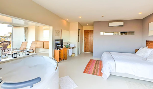 Imagem de um quarto de hotel espaçoso e moderno com cama confortável, TV, varanda com cadeiras, isolamento acústico e decoração aconchegante, ideal para hospedagem.