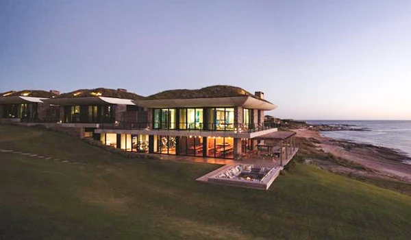 Imagem de uma moderna casa à beira-mar ao pôr do sol, com arquitetura sofisticada e vista para o oceano, ideal para quem busca luxo e conforto na praia.