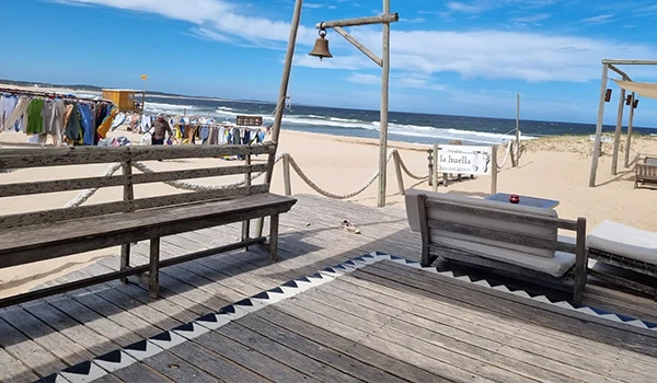 Cenário de praia com teto de madeira, bancos de madeir para descanso, roupas penduradas para secar e vista para o mar sob céu azul claro, ideal para lazer e relaxamento.  José Ignacio paradores e restaurantes.