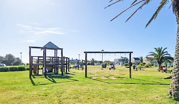 Imagem de um parque infantil ao ar livre com balanços, escorregador e áreas verdes sob céu azul, ideal para lazer e recreação em família.  José Ignacio paradores e restaurantes.