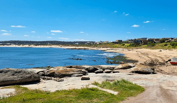 Praia com areia clara, pedras ao longo da orla e águas calmas sob céu azul com algumas nuvens, ideal para relaxar e apreciar a natureza na costa.  José Ignacio paradores e restaurantes.