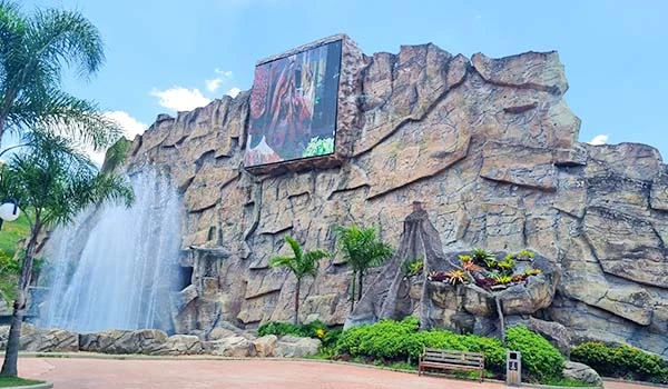 Fachada imponente com cascata em destaque, rodeada por vegetação exuberante e uma enorme pintura. Espetáculo de beleza na arquitetura.