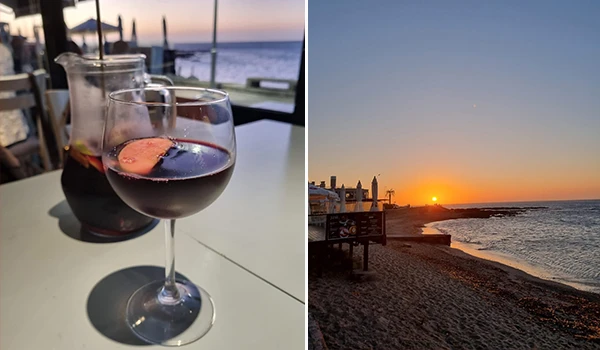 Duas taças de vinho tinto em uma mesa de restaurante com vista para o mar ao pôr do sol, criando uma atmosfera romântica e relaxante.