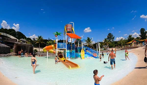 Parque aquático infantil com toboáguas coloridos, crianças se divertindo na água sob um céu azul claro. Uma ótima opção de lazer em família!