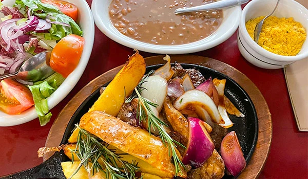 Prato de comida com ingredientes assados, incluindo cebolas roxas, abóbora, e temperos, acompanhado de salada de folhas verdes e molho, ideal para refeições nutritivas, no tradicional Bar do Leo.