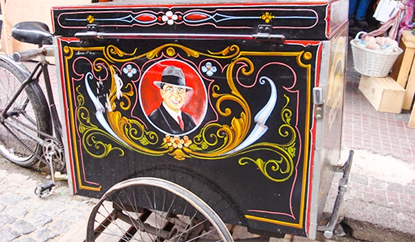 Imagem de um carrinho com pintura decorativa que inclui um retrato de um homem com chapéu, rodeado por detalhes coloridos e elementos artísticos. Viagem para Buenos Aires.