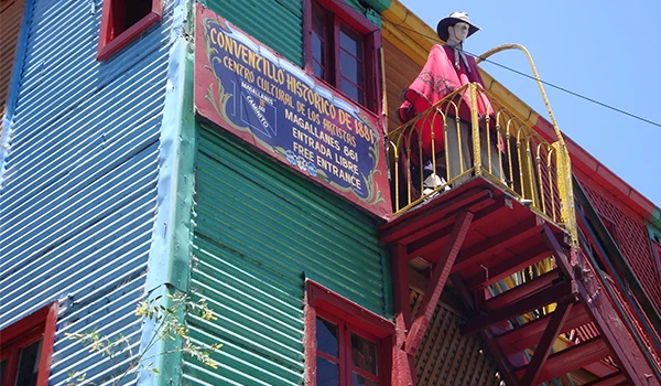 Casa fachada colorida, escada externa e uma placa histórica em Caminito, Viagem para Buenos Aires.