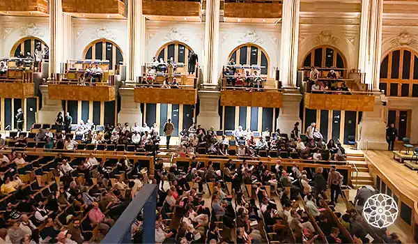 Imagem de um auditório lotado com várias pessoas assistindo a um evento cultural ou apresentação, com arquitetura elegante e iluminação quente, promovendo cultura e entretenimento. Dicas da Sala São Paulo.