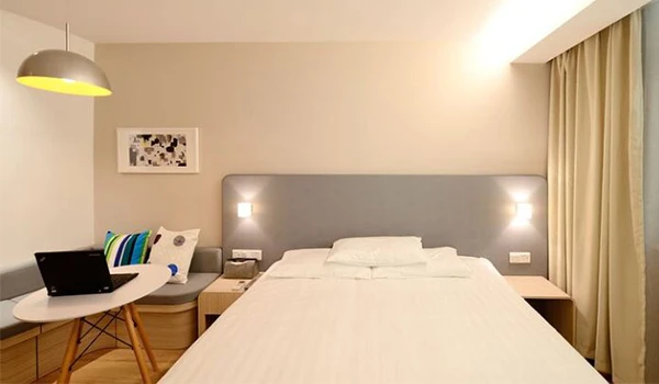 Quarto de hotel moderno com cama de casal, iluminação aconchegante, cortinas, mesa de trabalho, decoração simples e confortável, ideal para hospedagem.