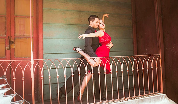 Casal de dança apaixonado performando uma rotina de tango em uma varanda com fundo de cores vibrantes, destacando a conexão e expressão artística.