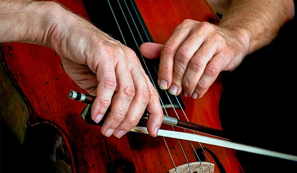 Mãos tocando violino com arco, destacando a técnica de execução musical.