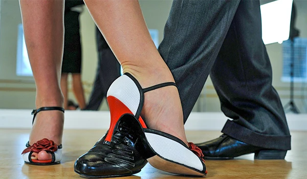 Mulher usando sapatos de dança de salão preto e branco com detalhes em vermelho, praticando uma dança coreografada ao lado de seu parceiro em um show de tango em Buenos Aires.