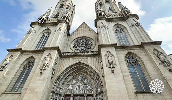 Fachada da Catedral de São Patrício em Nova York, com arquitetura neogótica em pedra clara, grandes janelas, rosácea central e detalhes ornamentais sob céu nublado