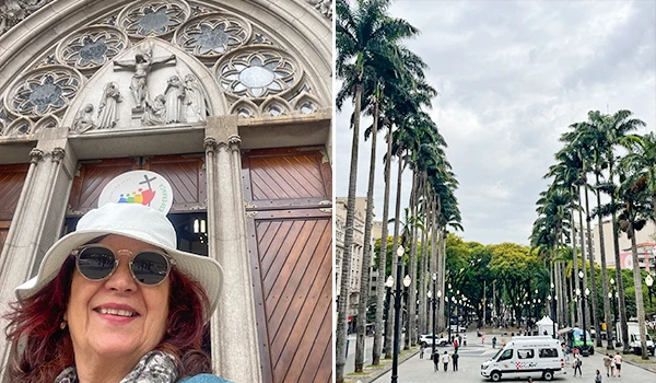 Imagem de uma mulher sorridente com chapéu e óculos escuros tirando uma selfie em frente a uma igreja histórica e uma praça com palmeiras ao fundo, em uma cidade pitoresca.