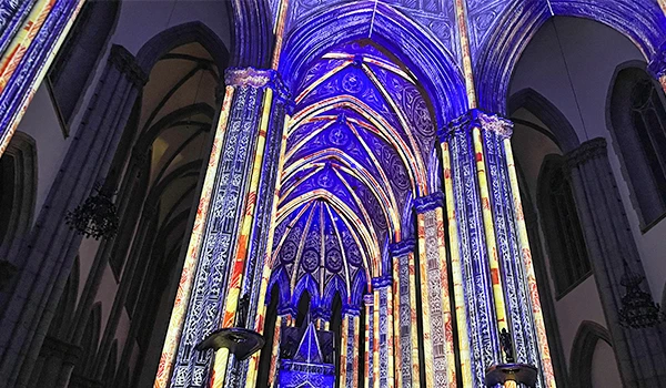 Interior de uma catedral iluminada com luzes coloridas em tons de azul e roxo, destacando detalhes arquitetônicos góticos.