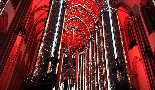 Interior de uma igreja ou catedral decorada com luzes de Natal e efeitos de iluminação vermelha, destacando as altas colunas e arquitetura gótica.