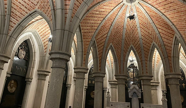 Interior da Catedral com abóbadas altas de tijolos aparentes, arcos de pedra e colunas, além de altar e vitrais ao fundo, em perspectiva ampla.  Cripta da Catedral da Sé.