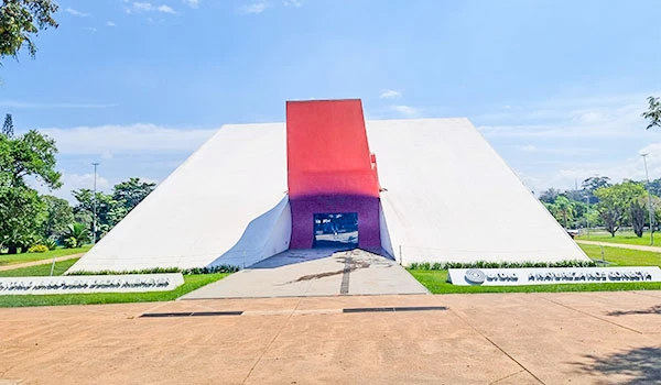 Imagem do auditório do Parque Ibirapuera, com sua arquitetura moderna, destaque para a estrutura com cores branca e vermelha e espaço ao redor bem cuidado.