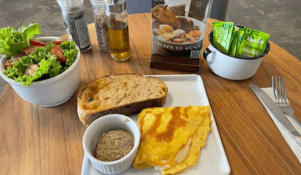 Refeição de café da manhã com pão, omelete, salada, azeite de oliva, sopa de lentilha e chá, ideal para um café da manhã saudável e nutritivo.