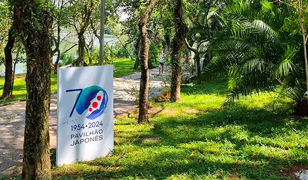 Pavilhão Japonês em um parque com árvores e espaço ao ar livre em homenagem aos 70 anos de relações brasileiras e japonesas, com sinalização comemorativa no Parque Ibirapuera.