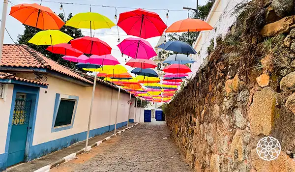 Cores vivas de guarda-chuvas coloridos decoram uma rua estreita de paralelepípedos, criando um cenário alegre e atraente para fotos em uma rua pitoresca. Dicas de Santana de Parnaíba.