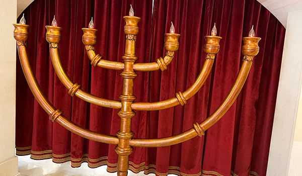 Menorá de sete braços em um ambiente decorado com cortinas vermelhas, simbolizando a tradição judaica e a luz.