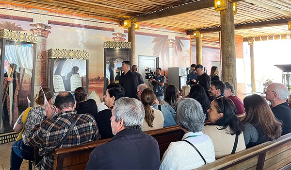 Imagem de um público assistindo a uma apresentação, com uma decoração temática no fundo e uma cena que evoca elementos culturais e históricos, durante a visita guiada ao Templo de Salomão.